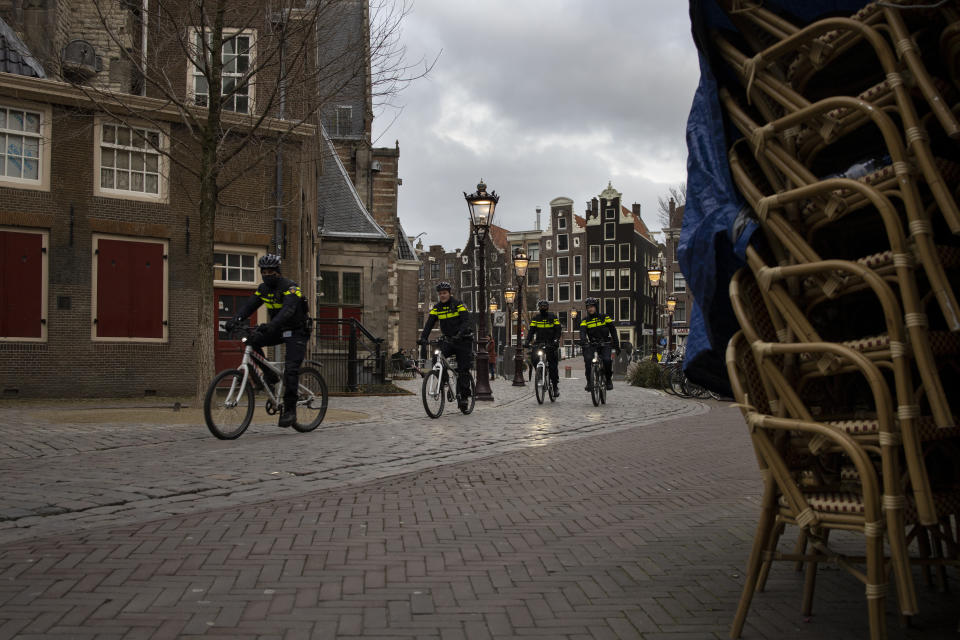 FILE - In this Jan. 14, 2021, file photo, police officers on bicycles pass stacked up terrace chairs outside a bar in the near-empty Red Light District in Amsterdam. The Dutch government this week extended by three weeks the tough lockdown in force since mid-December amid fears that coronavirus infection rates are not declining quickly enough and fears about a new more transmissible variant of the COVID-19 virus. (AP Photo/Peter Dejong)