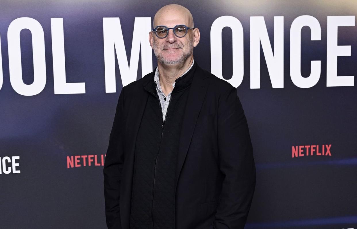 harlan coben, a man stands looking at the camera smiling, he wears glasses, a white shirt and black jacket