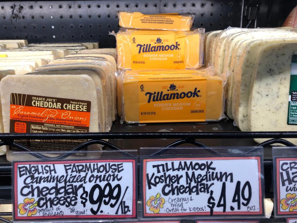A display of cheeses at Trader Joe's, including Tillamook cheddar cheese. The Tillamook price tag reads $4.49.