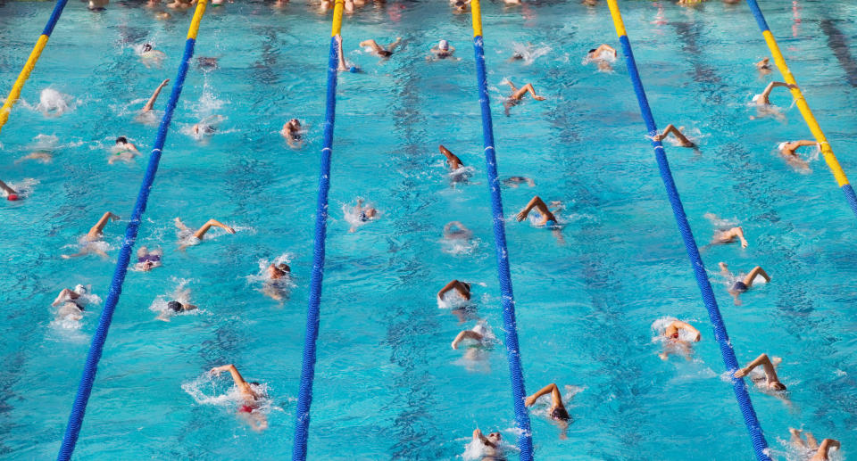 A swimming pool with dozens of people doing laps.