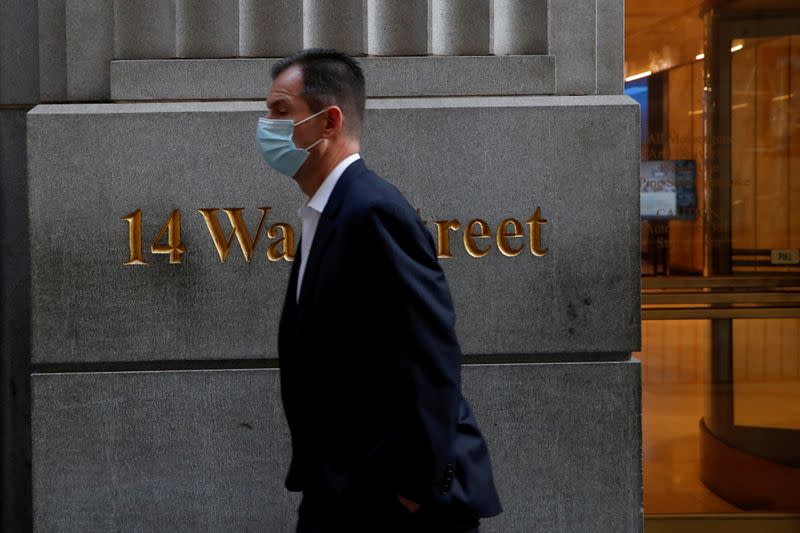 FILE PHOTO: A man wearing a protective face mask walks by 14 Wall Street, as the global outbreak of the coronavirus disease (COVID-19) continues, in the financial district of New York