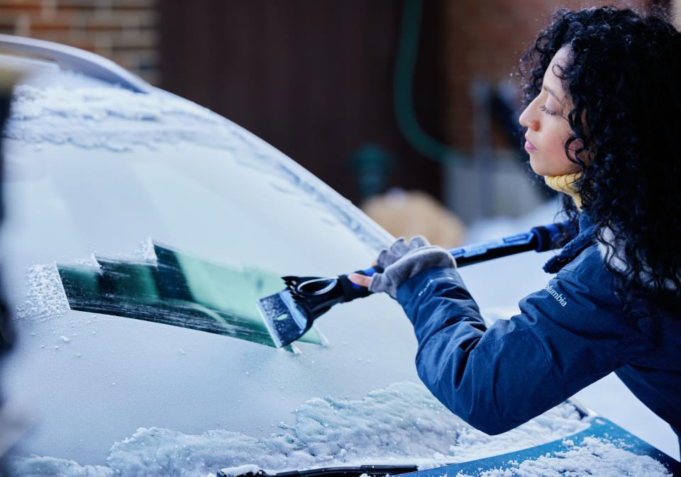 Woman clearing snow off her windshield using snow scraper and snow brush from Canadian Tire