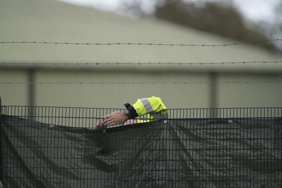 A member of security staff secures screens around the Manston immigration short-term holding facility located at the former Defence Fire Training and Development Centre in Thanet, Kent, England, Tuesday, Nov. 1, 2022. (Gareth Fuller/PA via AP)