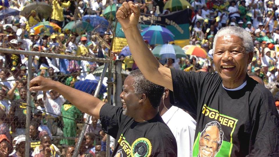 South African President Nelson Mandela (R) and Vice President Thabo Mbeki (L) greet the crowd from a pickup truck during an African National Congress meeting at Orlando Stadium in Soweto, March 28, 1999.