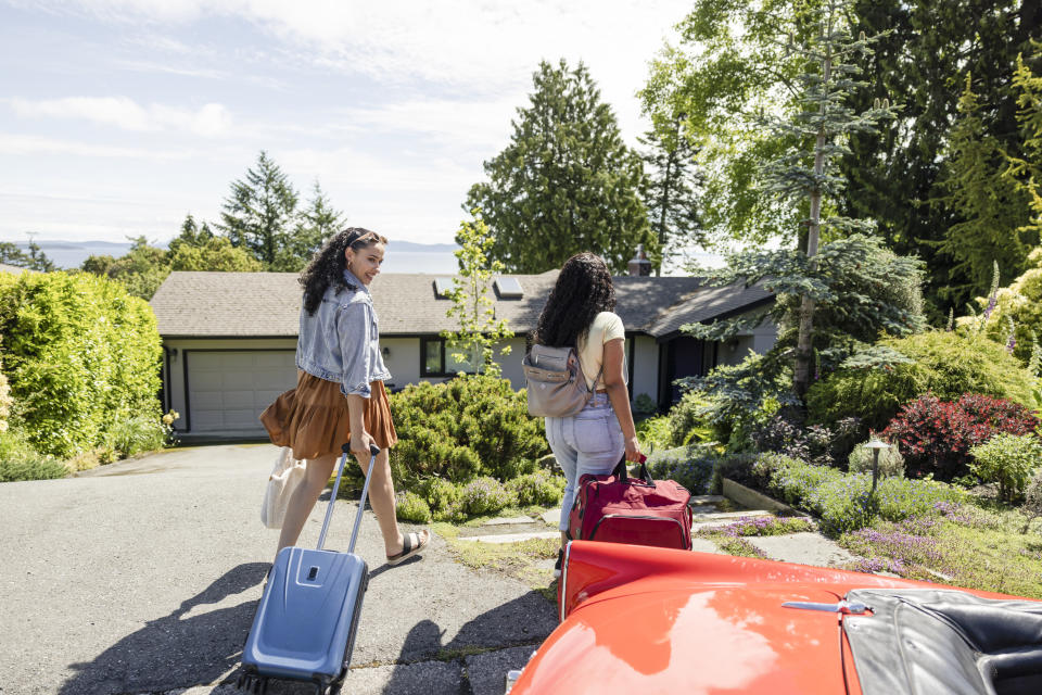 Young women friends with suitcase walking toward sunny vacation house rental