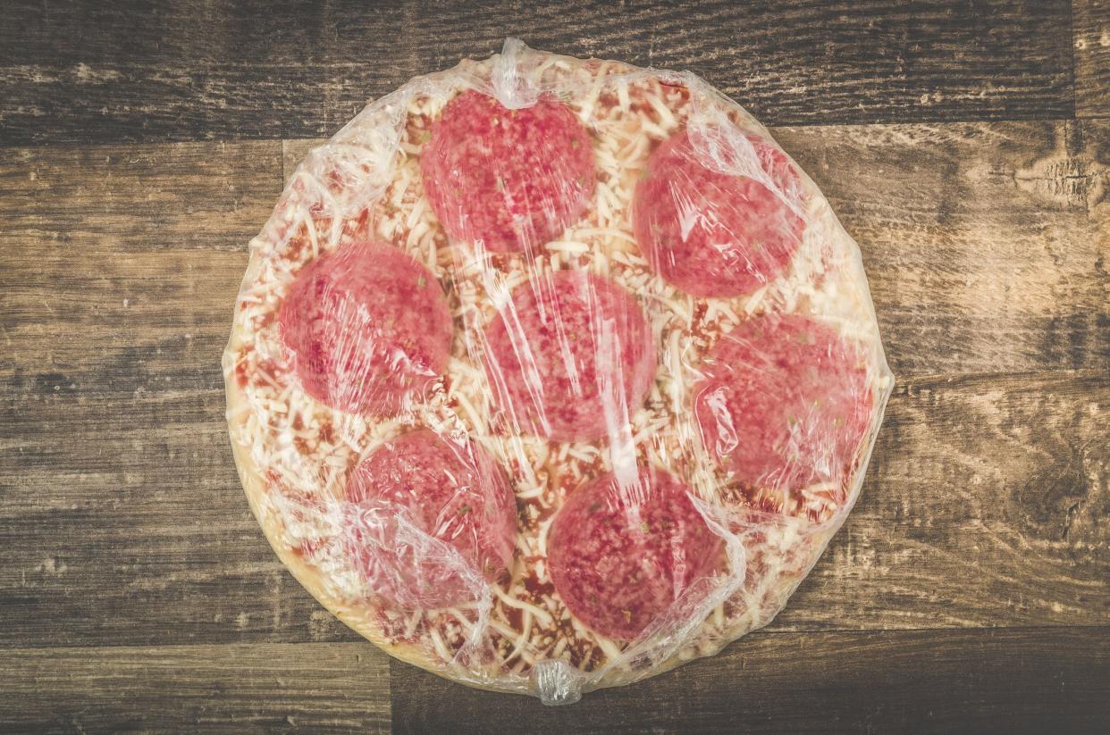 A professional DSLR photo of an raw mouth watering delicious Italian pizza with sausage salami and cheese in plastic on a wooden table. Studio shot with professional equipment. Soft vintage post processing for a lovely retro image effect.