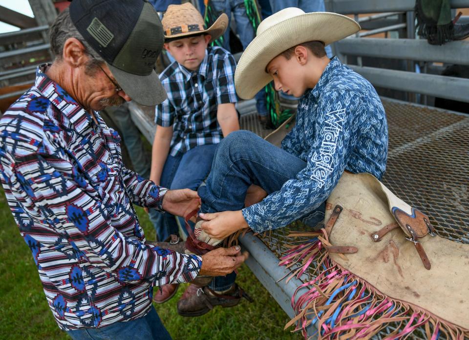 Homer "Buckshot" Morrison (left), grandfather of Trip Burley, helps Trip (right), prepare for his ride as friend Christian Bryant watches during the South Florida Mini Bull Tour Season Finals at the Fellsmere Riding Club arena on Saturday, Sept. 10, 2022, in Fellsmere. "We're taking him to Texas in three weeks to the nationals," Morrison said after getting Trip ready for his ride.