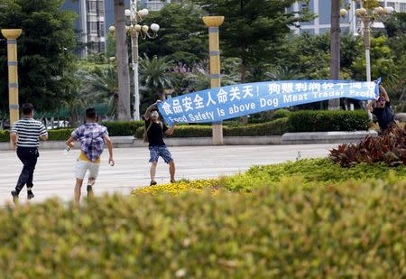 Men (L) whom animal right activists believe to be plain clothes policeman, run to snatch a placard from activists in front of a city hall in Yulin, Guangxi Autonomous Region, June 22, 2015, during a protest against the local dog meat festival. REUTERS/Kim Kyung-Hoon