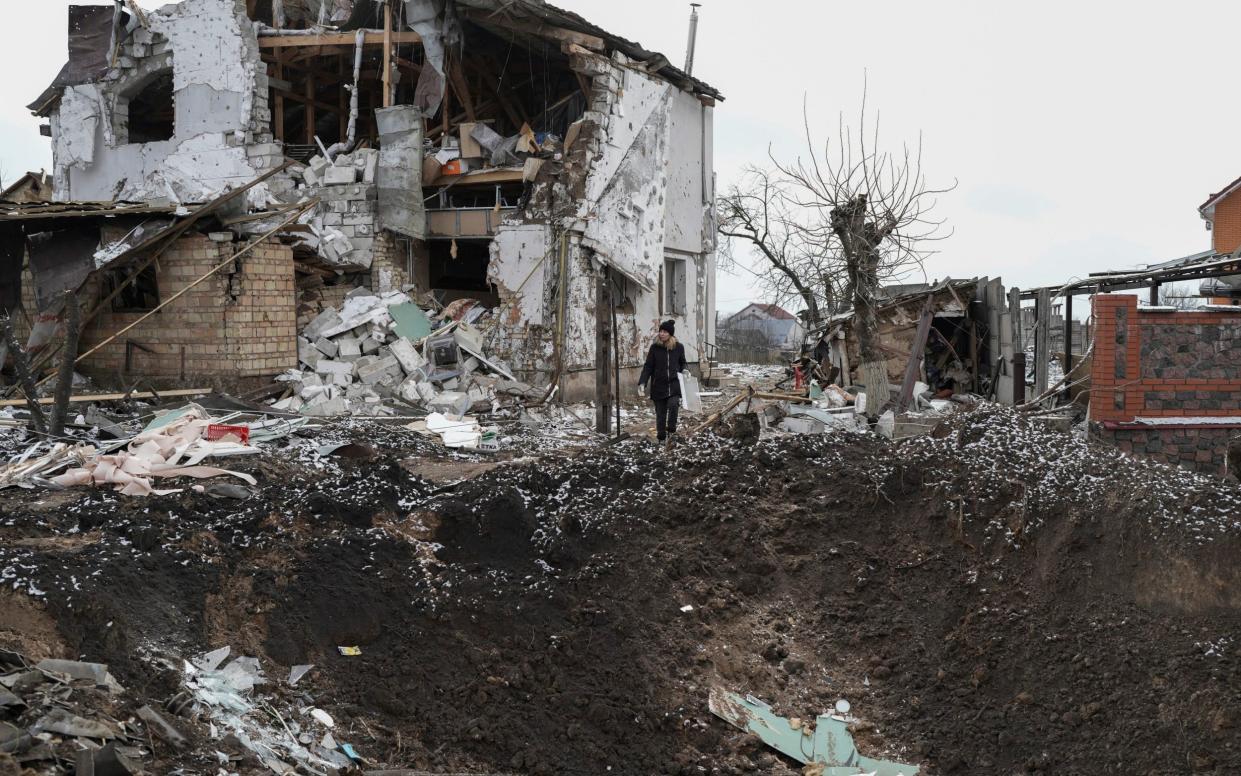 A woman stands on top of a crater next to a destroyed house after a Russian rocket attack in Hlevakha - Roman Hrytsyna/AP