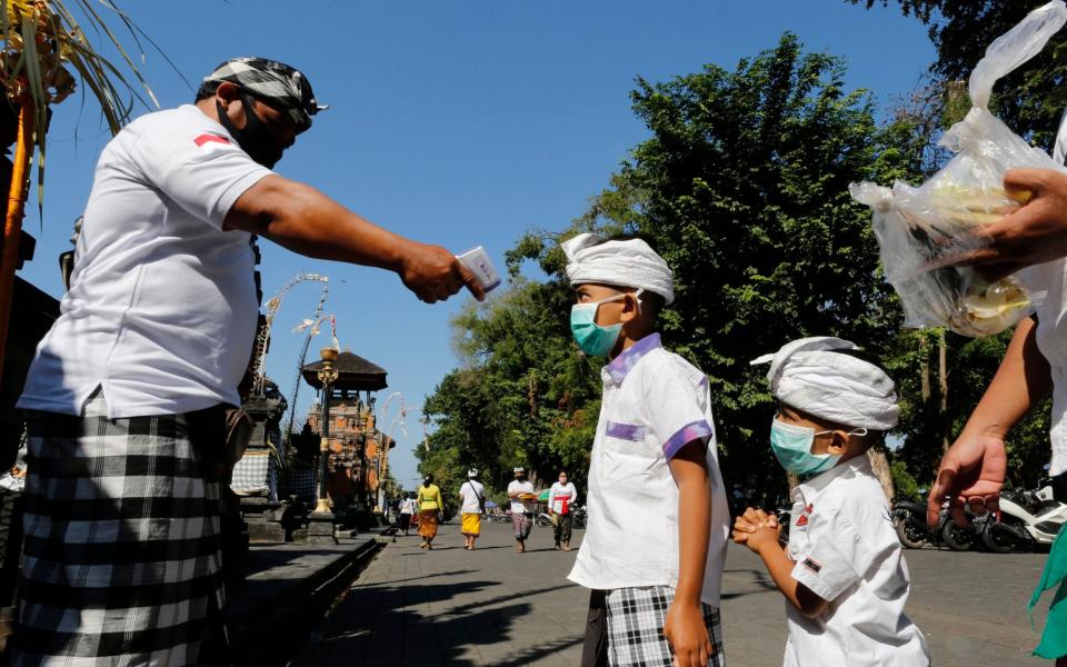 A security guard checks the body temperature of children at a temple  - AP