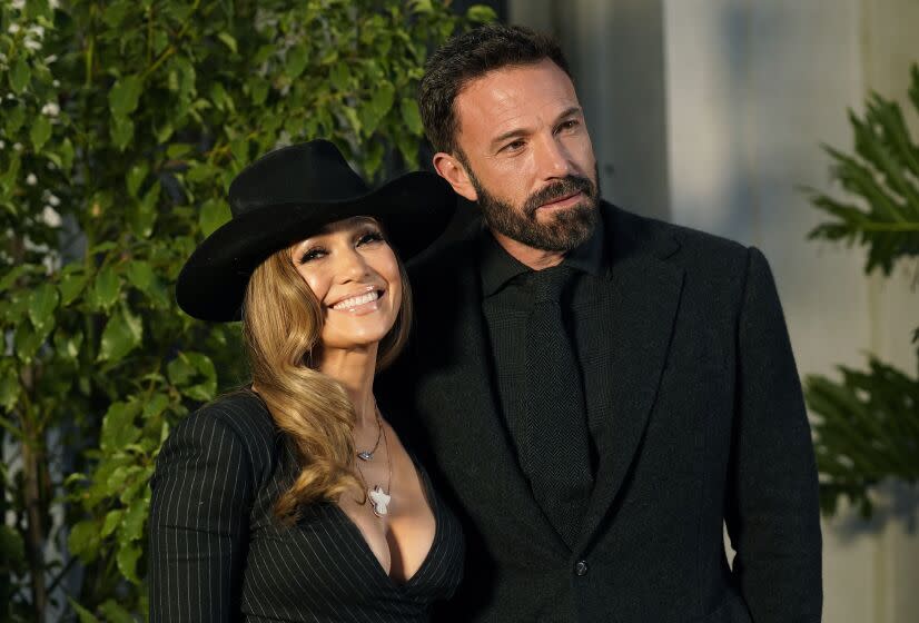 Jennifer Lopez in a black wide-brimmed hat and a black dress with a deep neckline next to Ben Affleck in a black suit