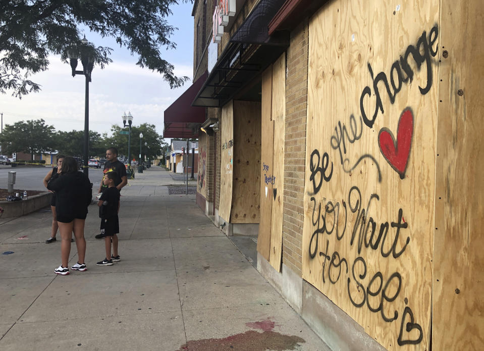 Residents stand in front of boarded-up businesses in Kenosha, Wis., Thursday, Aug. 27, 2020, days after protests of the police shooting of Jacob Blake turned violent and demonstrators set fire to a number of buildings. (AP Photo/Russell Contreras)