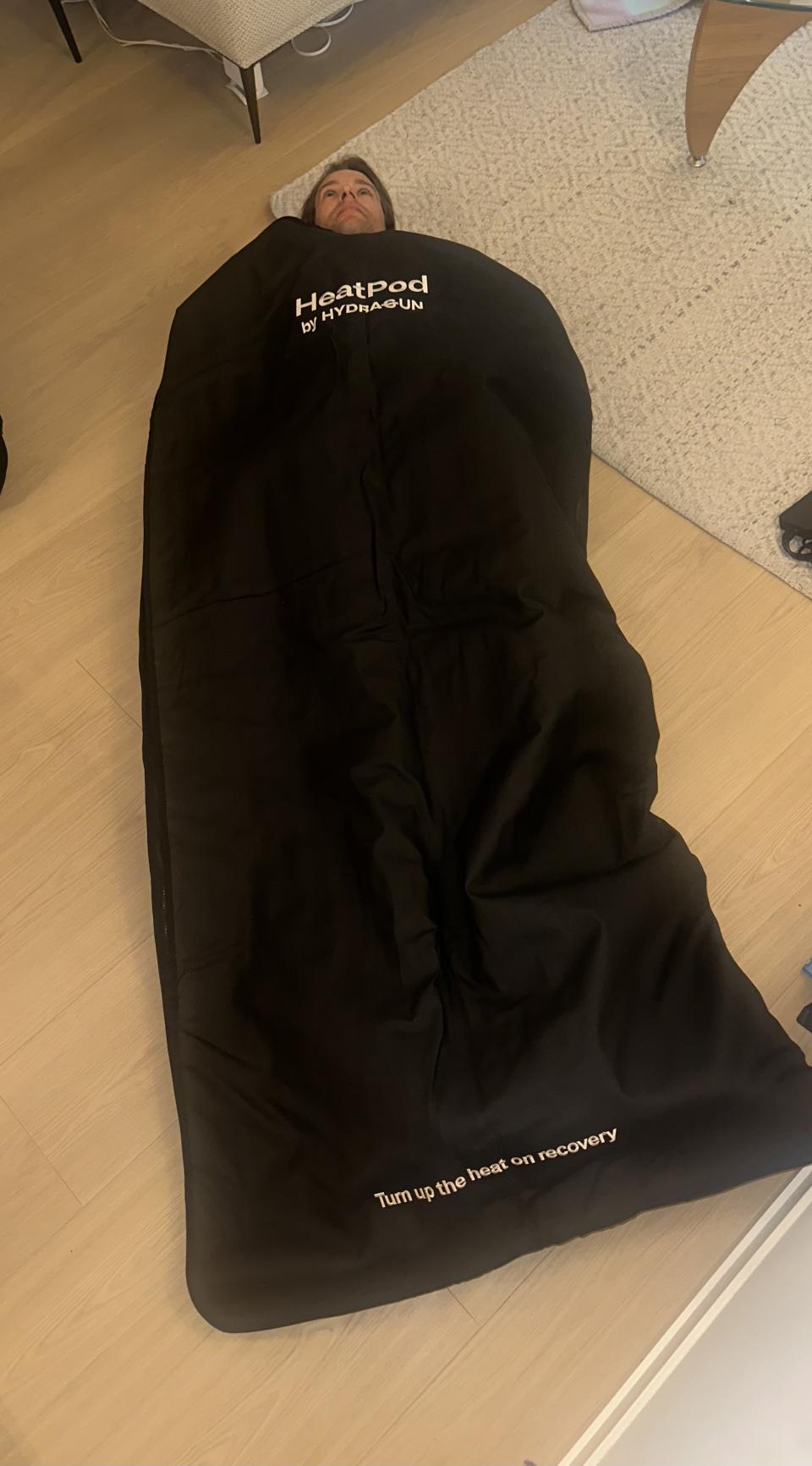 man laying inside black headpod bag, HeatPod Sauna Blanket 2 Infrared heat therapy for deep relaxation and rejuvenation