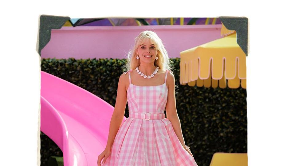 margot robbie as barbie in pink gingham dress in front of barbie dream house