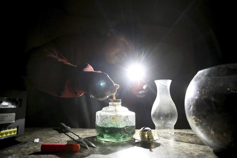 In this Wednesday, May 8, 2019 photo, Jimmie Long Jr. uses his cell phone flashlight to repair an oil lamp inside his Kaibwto home on the Navajo Reservation. Long and his wife, Miranda Haskie, were spending one last night without electricity in their home before being connected to the grid on Thursday, May 16, 2019. An ambitious project to connect homes to the electric grid on the country's largest American Indian reservation is wrapping up. Utility crews from across the U.S. have volunteered their time over the past few weeks to hook up about 300 homes on the Navajo Nation. (AP Photo/Jake Bacon)