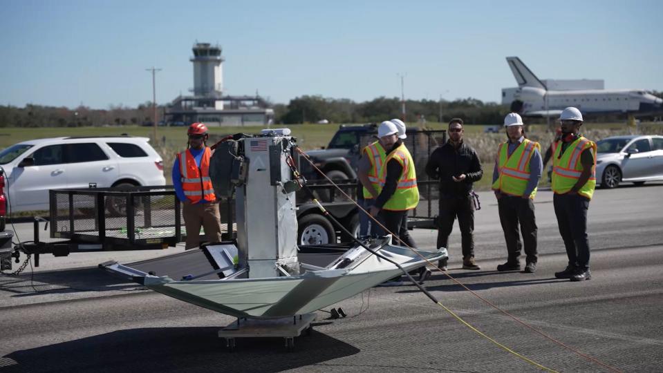 a device like an upside-down umbrella lays on a black asphalt runway