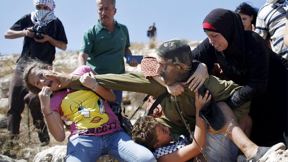 A group of Palestinian women begin grappling with the soldier and punching him repeatedly and biting his hand while he holds down the boy. Photo: AFP