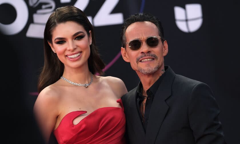 woman with long brown hair worn down in red strapless dress smiles next to man with short hair, black sunglasses and suit