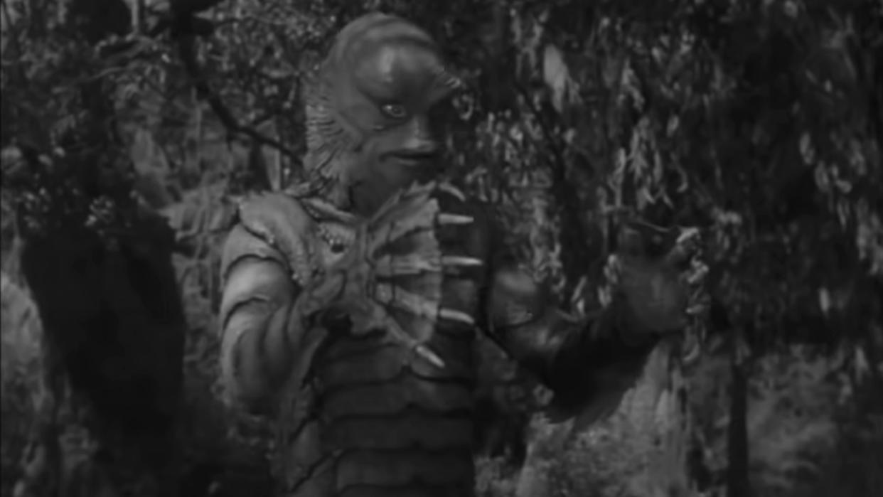  Ricou Browning in costume as the Creature from the Black Lagoon, walking forward with his hands out. 