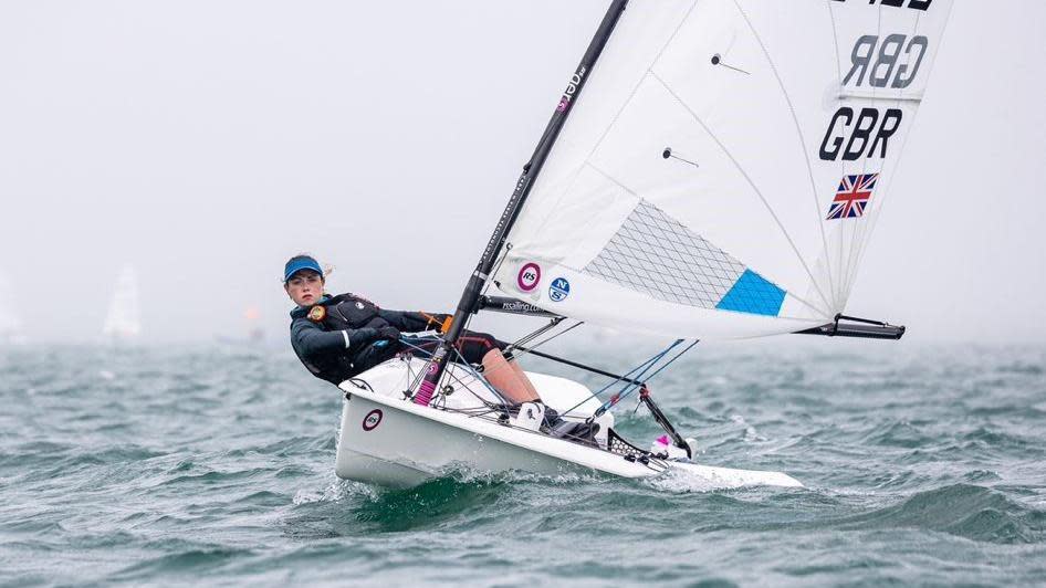 Francesca is leaning backwards off the side of a boat, holding the sail. She looks focused as she sails.