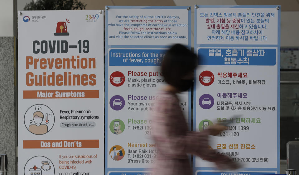 A woman wearing a face mask walks near a banner showing precautions against the new coronavirus at an exhibition and convention center in Goyang, South Korea, Friday, June 12, 2020. (AP Photo/Lee Jin-man)