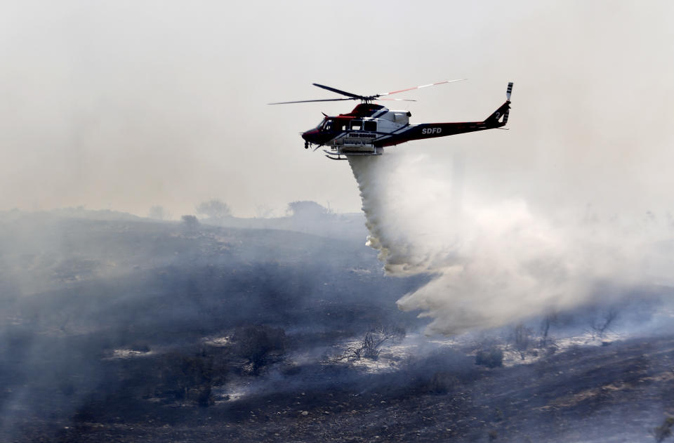 A helicopter attacks a wildfire burning in the north county of San Diego Tuesday, May 13, 2014, in San Diego. Wildfires pushed by gusty winds chewed through canyons parched by California's drought, prompting evacuation orders for more than 20,000 homes on the outskirts of San Diego and another 1,200 homes and businesses in Santa Barbara County 250 miles to the north. (AP Photo)