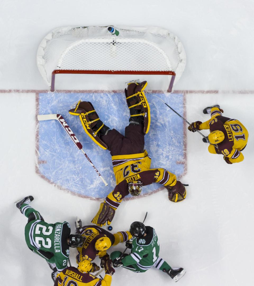 Minnesota's Adam Wilcox, top center, reaches for the puck with Gabe Guertler, center, tryings to keep North Dakota's Andrew Panzarella, left, and Colten St. Clair, right, away during the first period of an NCAA men's college hockey Frozen Four tournament game on Thursday, April 10, 2014, in Philadelphia. (AP Photo/Chris Szagola)