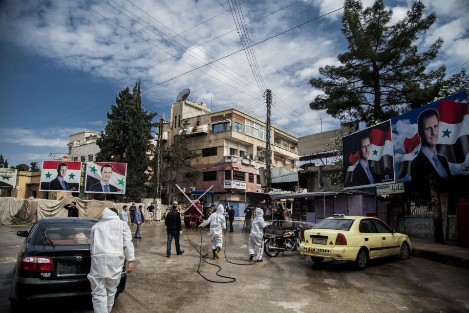 Workers disinfect the streets to prevent the spread of coronavirus in Qamishli, Syria, Tuesday, March 24, 2020. Posters show Syrian President Bashar Assad. (AP Photo/Baderkhan Ahmad)