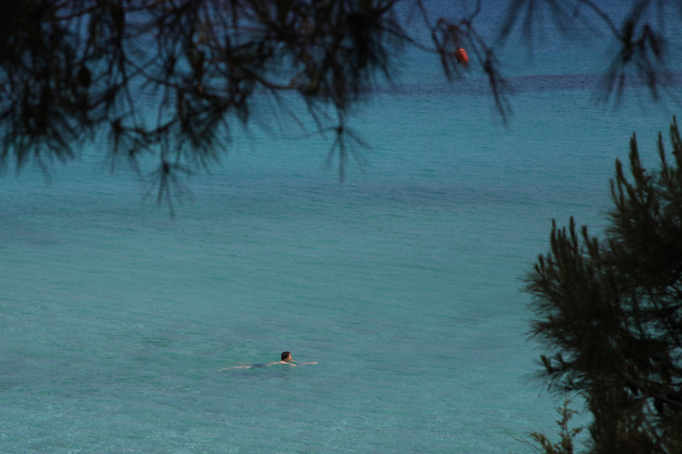 FILE - In this Sunday, May 10, 2020 file photo, a lone person swims through the clear waters of 'Konnos' beach in Ayia Napa, Cyprus. Cyprus government spokesman Kyriakos Koushos said on Tuesday, Oct. 13, 2020, that the Cabinet accepted a recommendation by the minsters of the interior and finance to cancel altogether the "golden passport" program that has netted billions of euros over several years. Koushos said the decision was based on the Cyprus Investment Program's "long-standing weaknesses, but also the abuse" of its provisions. (AP Photo/Petros Karadjias, File)