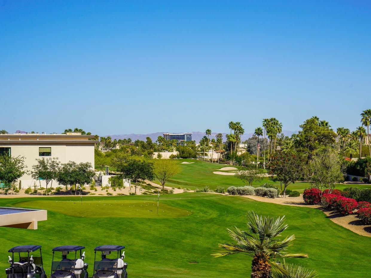 A golf course lined with palm trees with mountains in the background, clear blue skies