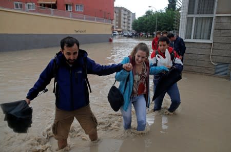 People wade through a flooded street close to the overflowing Segura river as torrential rains hit Orihuela