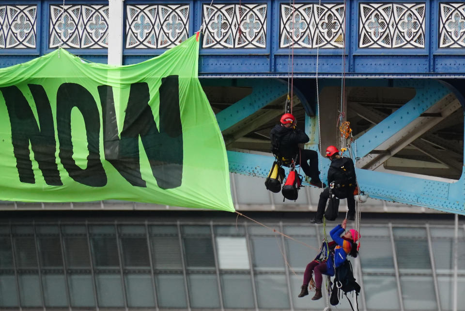 Police officers work to remove activists from Extinction Rebellion who are hanging from suspension cords beside a giant banner that reads 