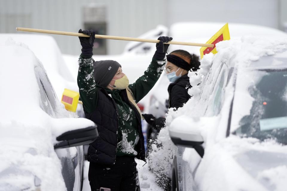 Renee Yanke, foreground, and Rosely Collado clean of cars at the Haddad Nissan dealership in Pittsfield, Mass., after a snowstorm hit the East coast, Tuesday, Feb. 2, 2021. (Ben Garver/The Berkshire Eagle via AP)