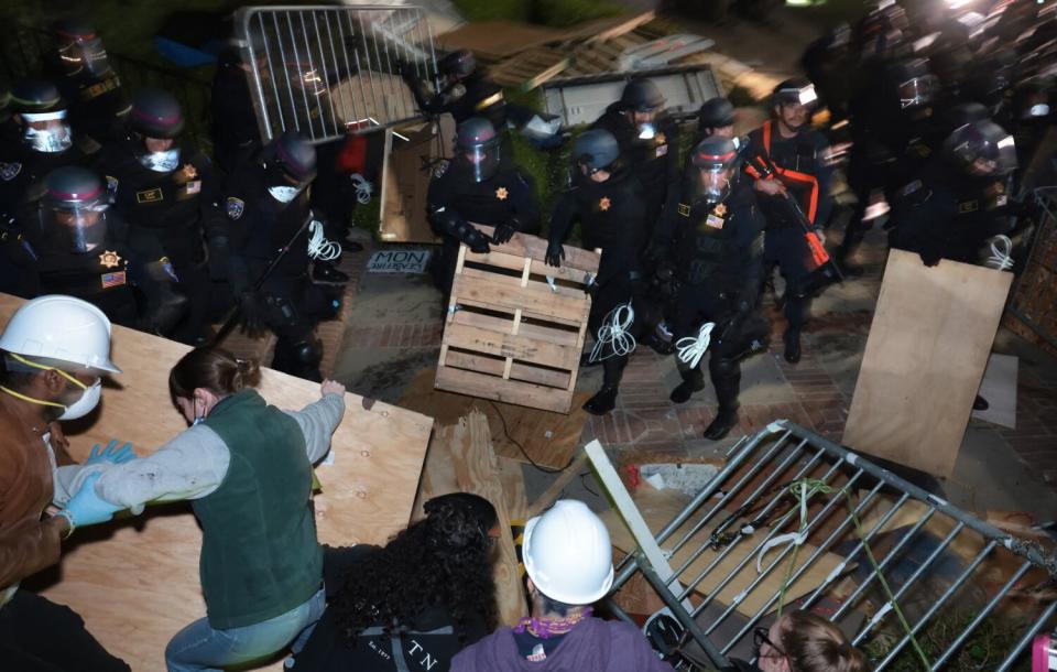 Police break up a camp, picking up items. Some other people grab items too.