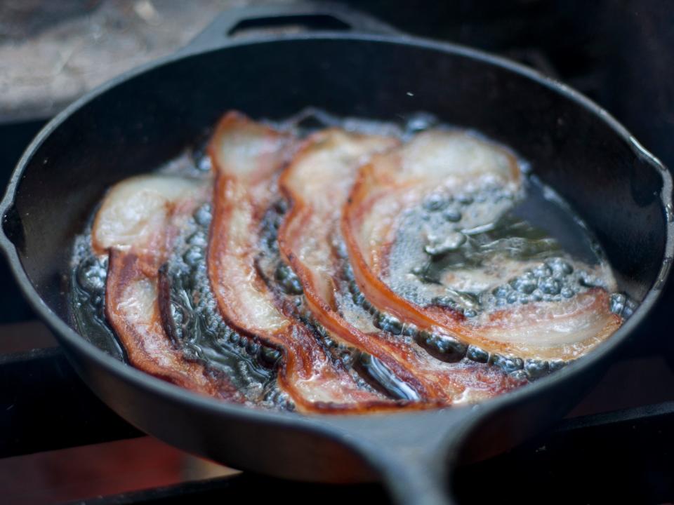 Four strips of bacon cooking in black pan on stove