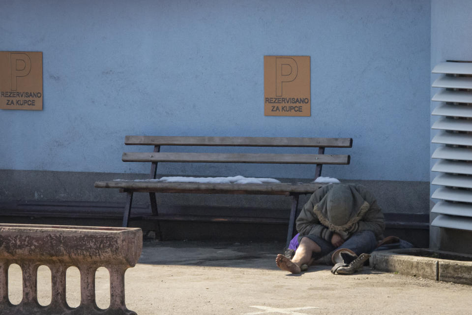 A migrant sits on the pavement to warm up outside the Miral camp, in Velika Kladusa, Bosnia, Wednesday, April 7, 2021. Bosnia is seeing a rise in coronavirus infections among migrants and refugees living in its camps, as it struggles to cope with one of the Balkans' highest COVID-19 death and infection rates among the general population.(AP Photo/Davor Midzic)