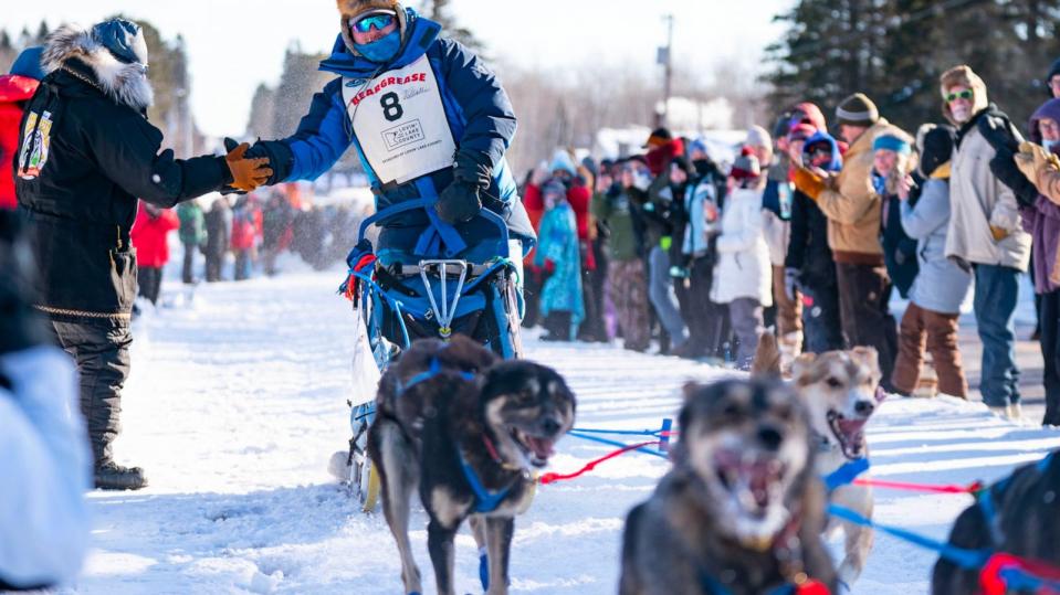 PHOTO: Ero Wallin slaps the hands of attendees as his sled dog team takes off from the start line of the John Beargrease Sled Dog Marathon Jan. 29, 2023, outside Billy's Bar in Duluth, Minn. (Alex Kormann/Star Tribune via Getty Images)