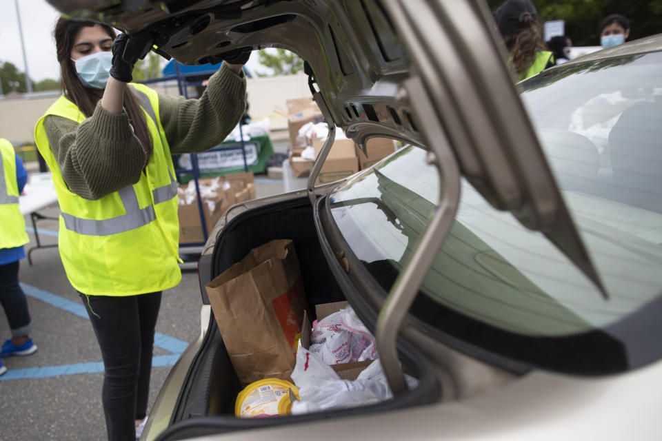 In this Thursday, May 28, 2020, photo, a volunteer places groceries in the trunk of a car during a food distribution drive sponsored by Island Harvest Food Bank in Valley Stream, N.Y. (AP Photo/Mary Altaffer)