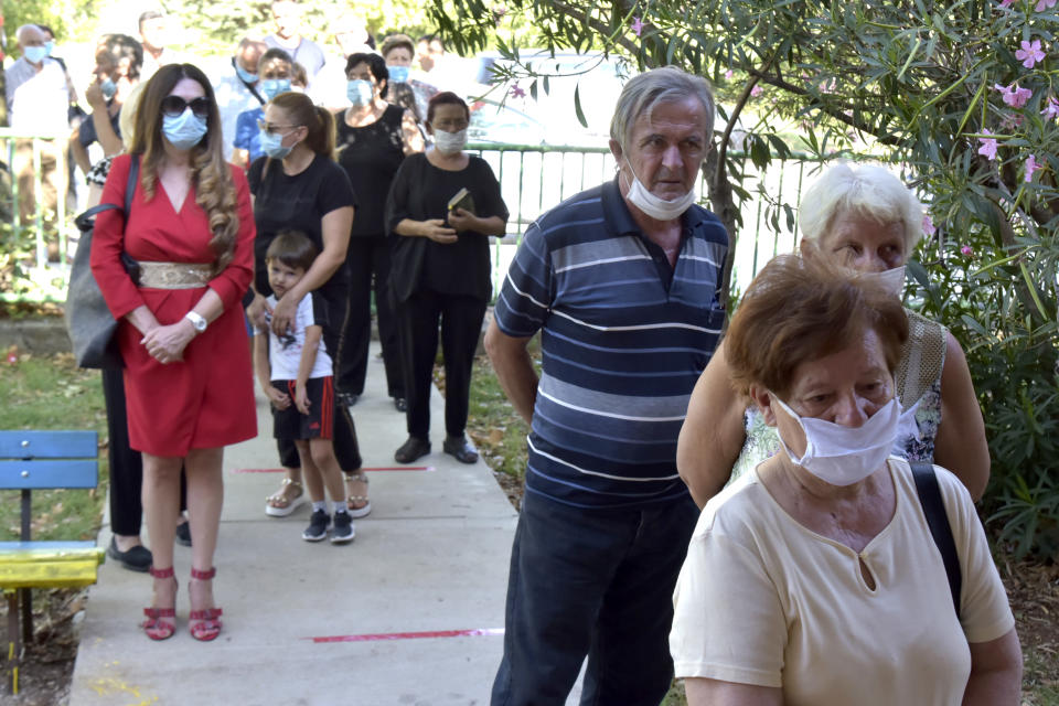 People wearing face masks wait in line at a poling station in Podgorica, Montenegro, Sunday, Aug. 30, 2020. Voters in Montenegro on Sunday cast ballots in a tense election that is pitting the long-ruling pro-Western party against the opposition seeking closer ties with Serbia and Russia. The parliamentary vote is marked by a dispute over a law on religious rights that is staunchly opposed by the influential Serbian Orthodox Church. (AP Photo/Risto Bozovic)