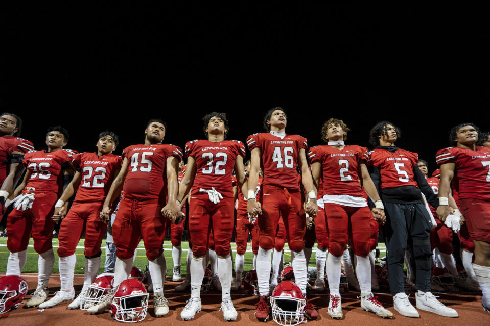 The Lahainaluna High School football team hold hands to thank the fans after a game Saturday, Oct. 21, 2023, in Lahaina, Hawaii. Lahainaluna’s varsity and junior varsity football teams are getting back to normal since the devastating wildfire in August. (AP Photo/Mengshin Lin)