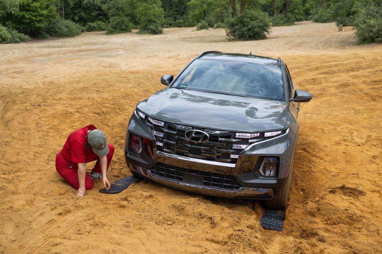 a person working placing traction boards in front of a car while in a sand pit