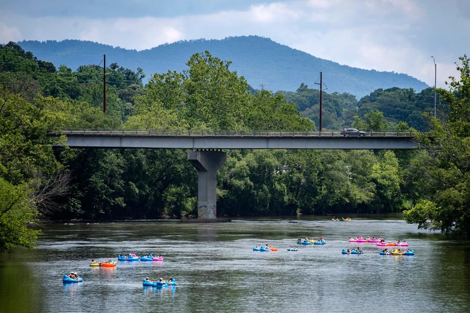 Several groups of people float toward the Craven Street Bridge on the French Broad River in rented tubes in July 2020.