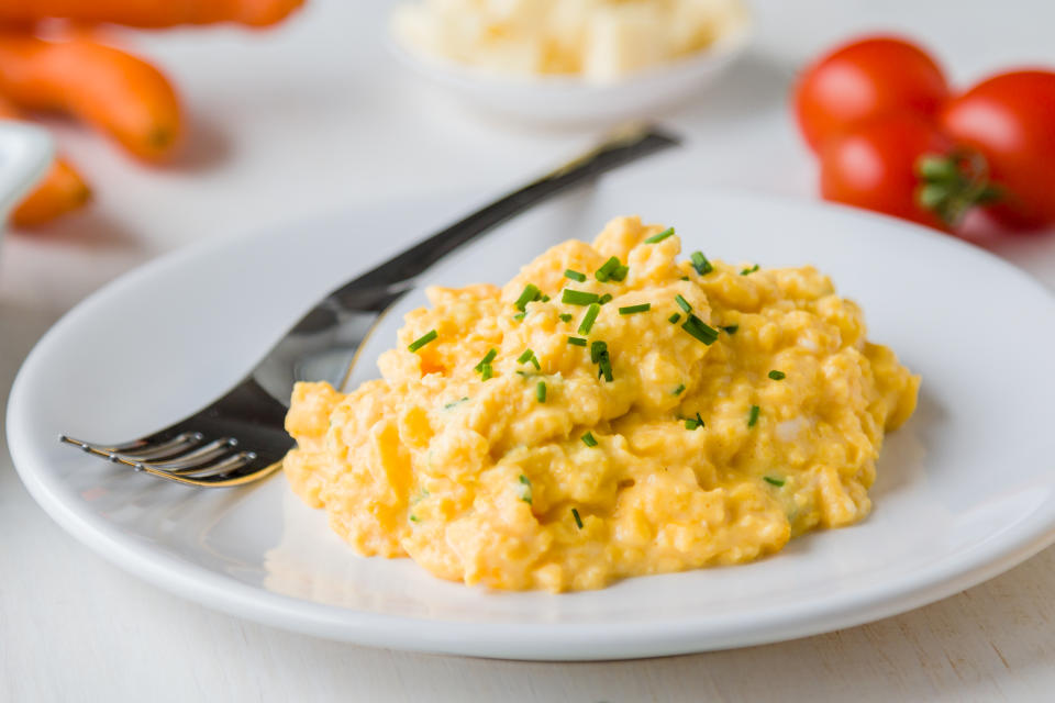 Scrambled eggs on white plate with a fork on a breakfast table with tomatoes