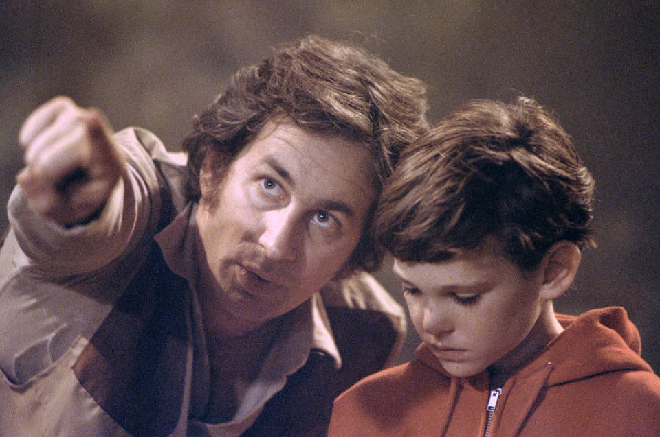 Steven Spielberg points while speaking to a young Henry Thomas during the filming of a scene. Thomas is looking down, listening attentively