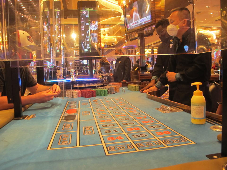 This May 3, 2021 photo shows a bottle of hand sanitizer, plexiglass barriers and face masks in use during a game of roulette at the Hard Rock casino in Atlantic City N.J. On May 24, 2021, New Jersey gambling regulators released figures showing that the Atlantic City casinos' first quarter earnings more than tripled this year compared to the same period last year, when the COVID19 pandemic wiped out half of March.(AP Photo/Wayne Parry)