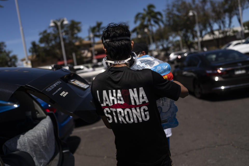 Ken Alba, a Lahaina, Hawaii, resident, carries a bag of ice at a food and supply distribution center set up in the parking lot of a shopping mall in Lahaina, Hawaii, Thursday, Aug. 17, 2023. The blazes incinerated the historic island community of Lahaina and killed more than 100 people. (AP Photo/Jae C. Hong)