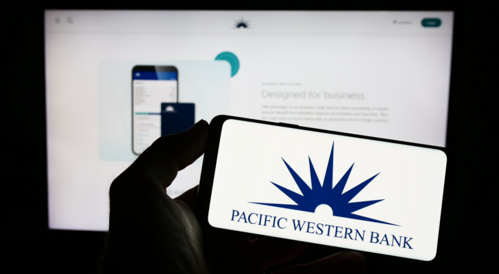 Person holding mobile phone with logo of American banking company PacWest Bancorp (PACW) on screen in front of business web page. Focus on phone display. Unmodified photo