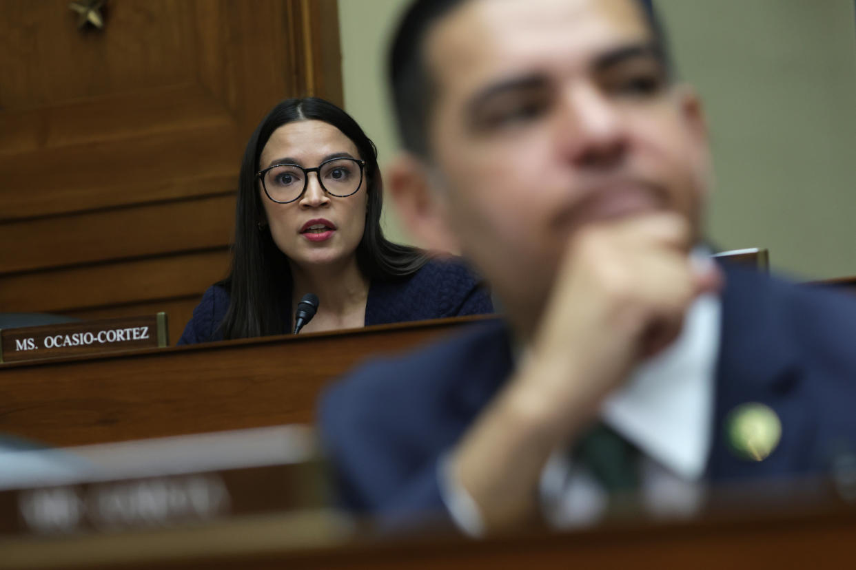 Rep. Alexandria Ocasio-Cortez, in glasses, listens intently.