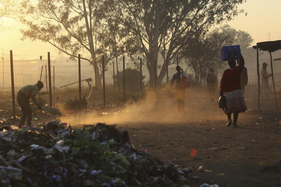 A man sweeps a path near a dumpsite in Harare, Thursday, Aug, 8, 2019. Many Zimbabweans who cheered the downfall of longtime leader Robert Mugabe two years ago have found the country's economy even worse than before.(AP Photo/Tsvangirayi Mukwazhi)