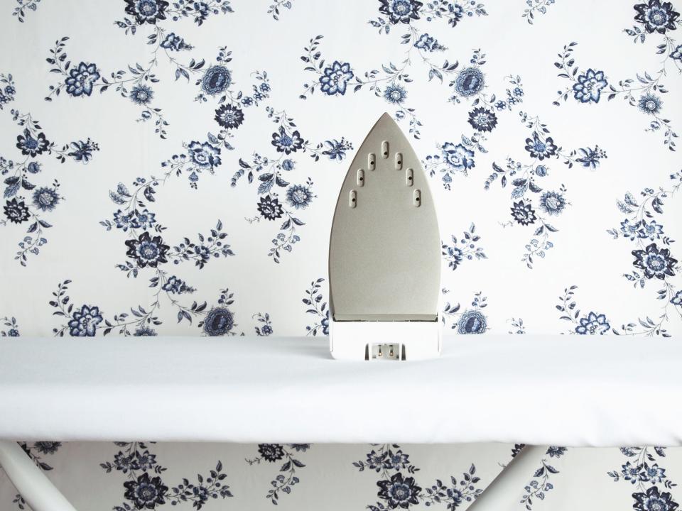 An iron sitting on an ironing board against a backdrop of floral wallpaper